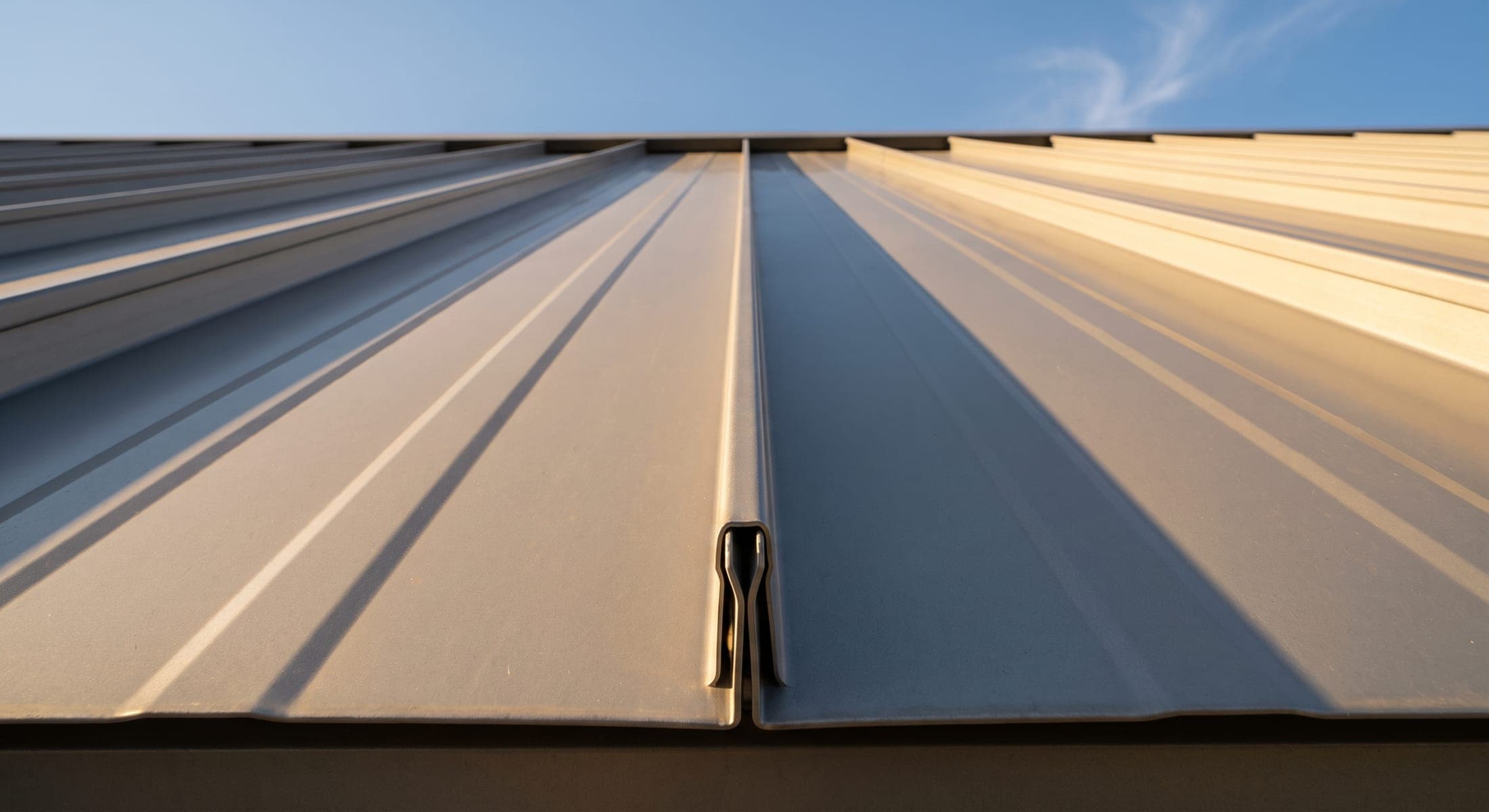 Extreme low-angle view looking up a standing-seam aluminum roof panel, showing the double-lock seam profile against a clear sky